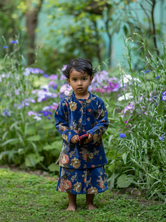 A child wearing a navy blue kurta with floral patterns, standing in a garden.